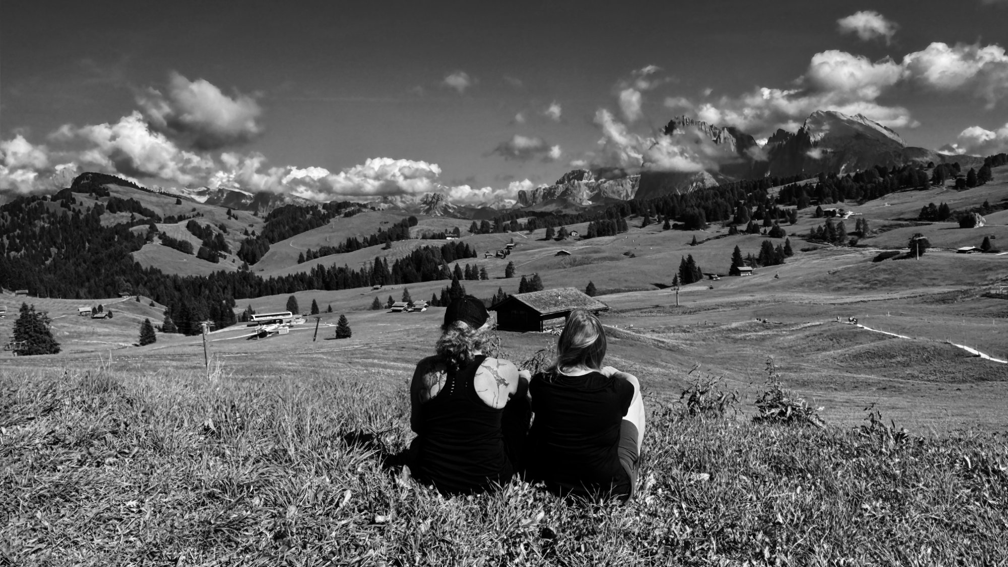 Zwei Freundinnen sitzen auf einer Bergwiese und blicken in die Weite